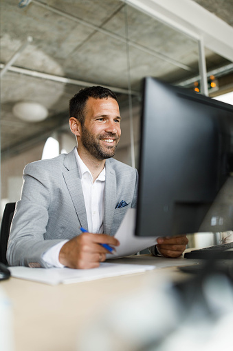 Happy businessman reading an e-mail while working on desktop PC